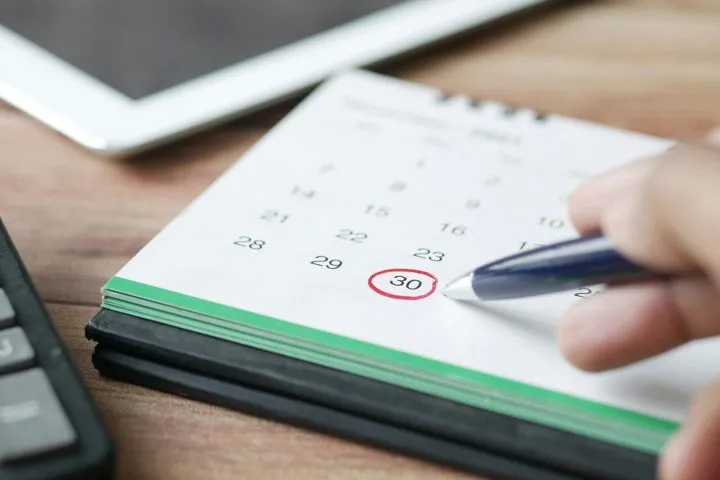 A hand circling a date on a paper calendar