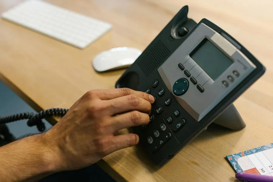 A hand dialling a number on a desk phone