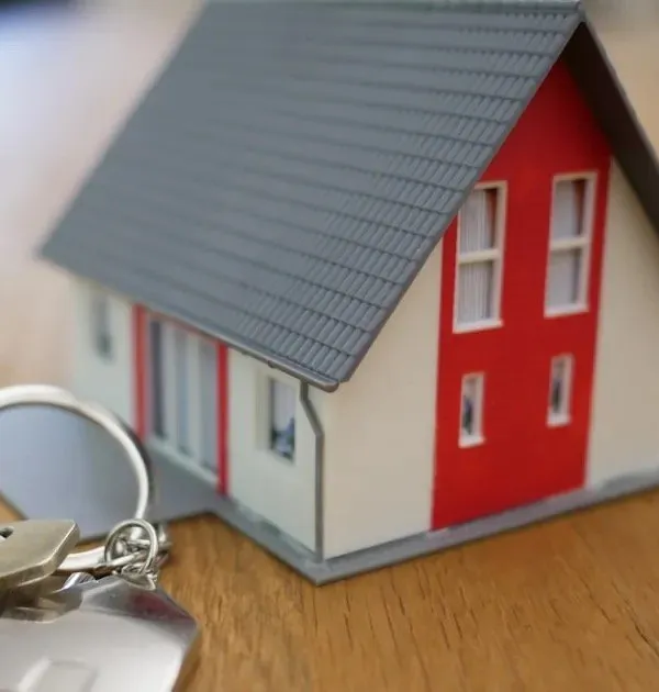 A small model house with a set of keys on a desk